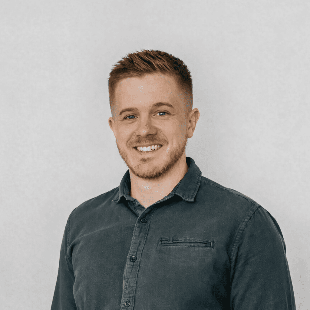 Professional headshot of a brunette woman in a white shirt, arms crossed, on a clean minimal background.