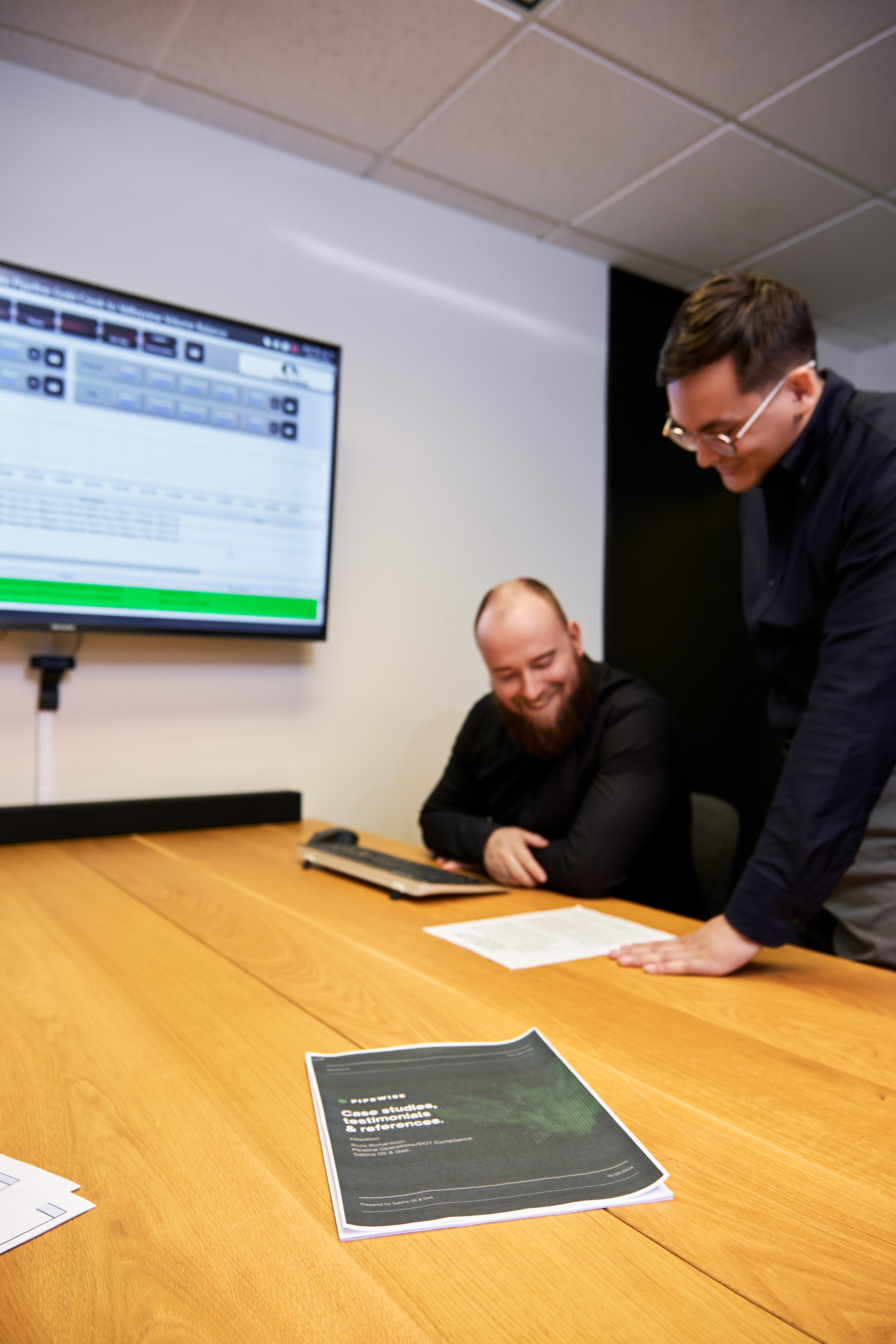 Black and white image of people working at a table with laptops, showing hands gesturing during discussion of digital content displayed on screens, with fabrica® logo in the corner.