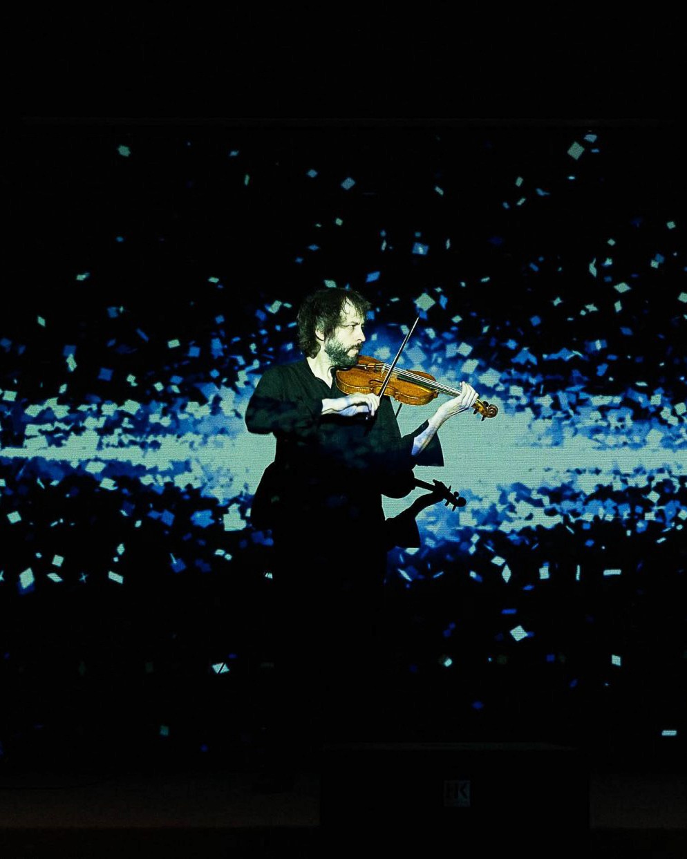 Man playing violin with blue digital texture projected on it.