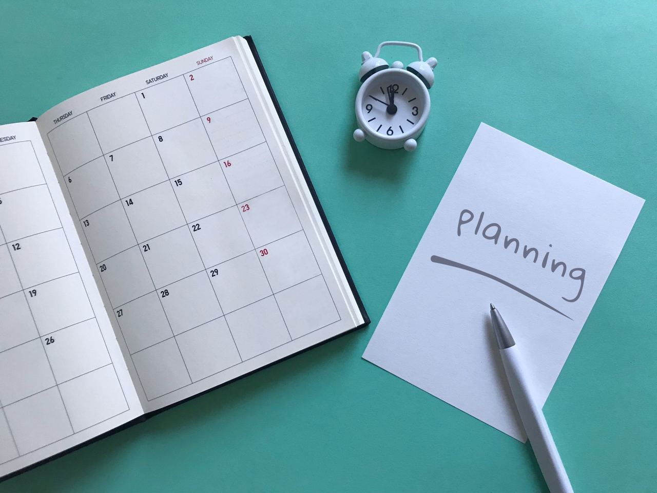 「Planning」と書かれたメモと月間カレンダー、目覚まし時計。現状把握から月次の維持まで進めるAIO対策のロードマップを表す