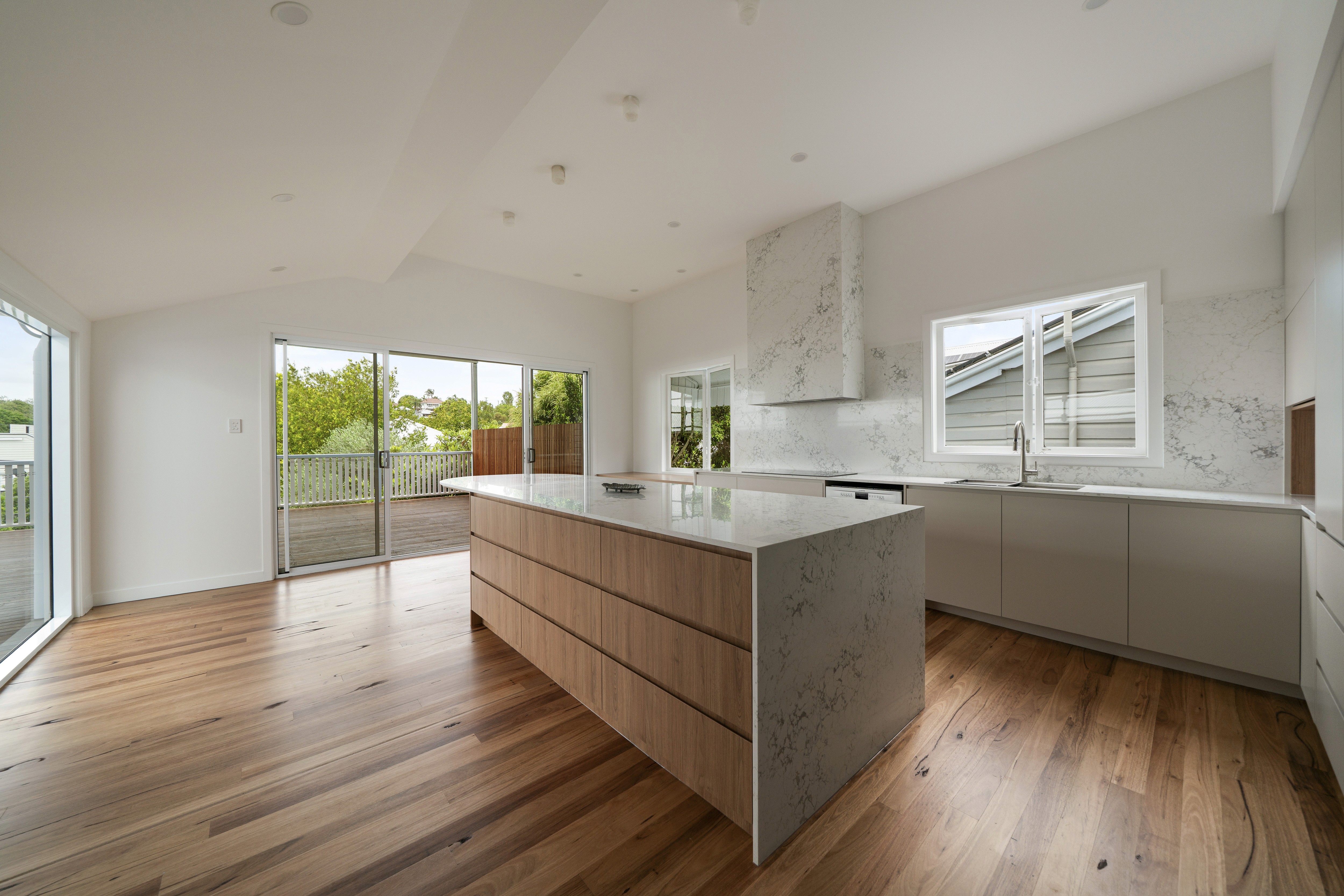 Upper level of a raised Queenslander in West End, Brisbane, opened up into a kitchen and living area with a timber island, stone benchtop and doors to the deck