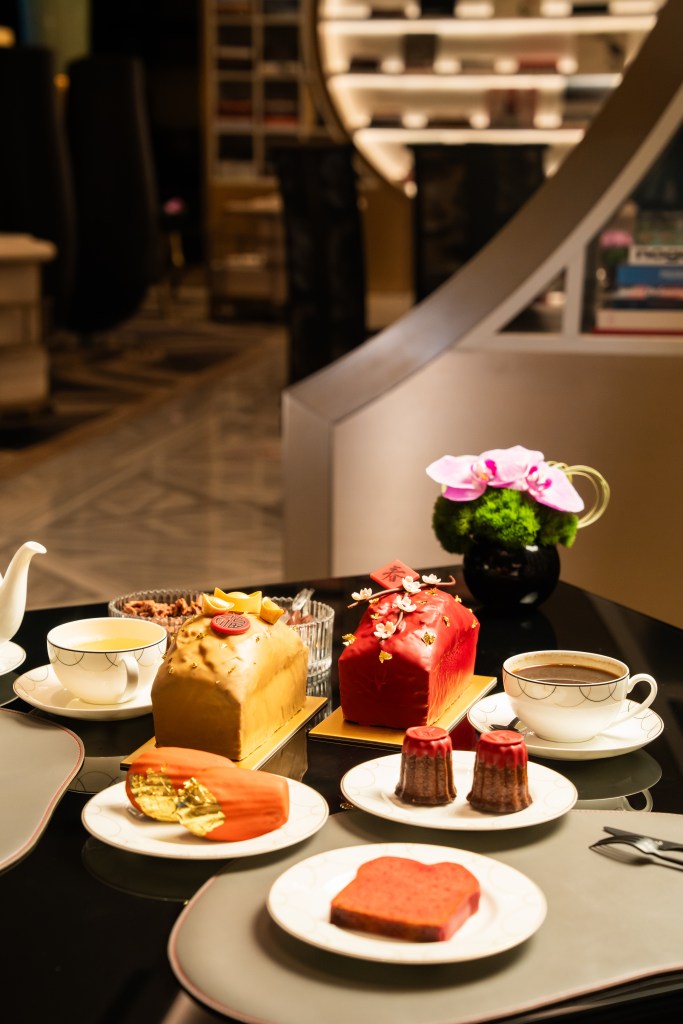 An assortment of elegant desserts including decorative cakes, a tea set, and a potted orchid displayed on a black table.