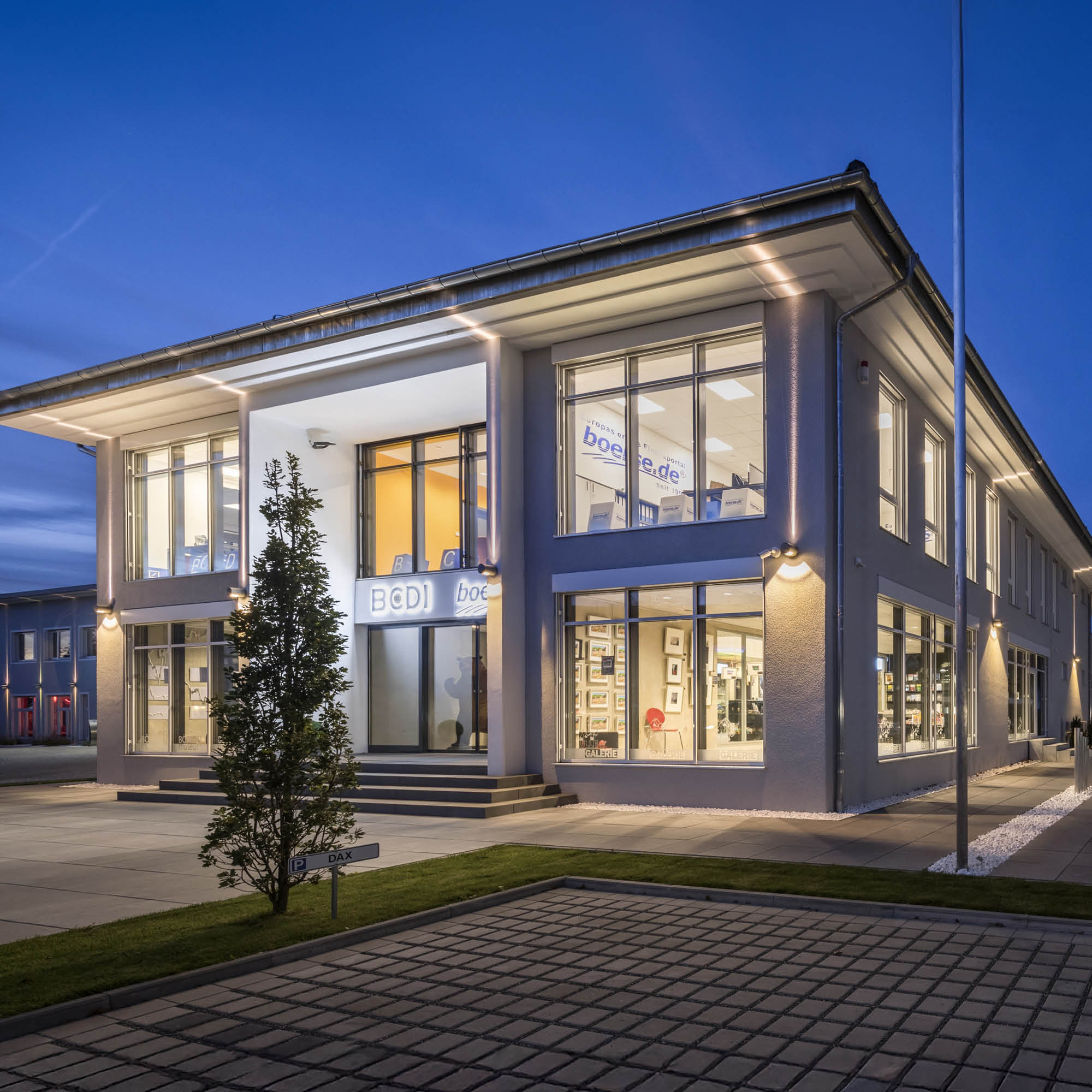 Modernes Gebäude der BoConcept-Galerie bei Nacht mit deutlicher Beschilderung und beleuchteten Fenstern sowie einem davorstehenden Baum.
