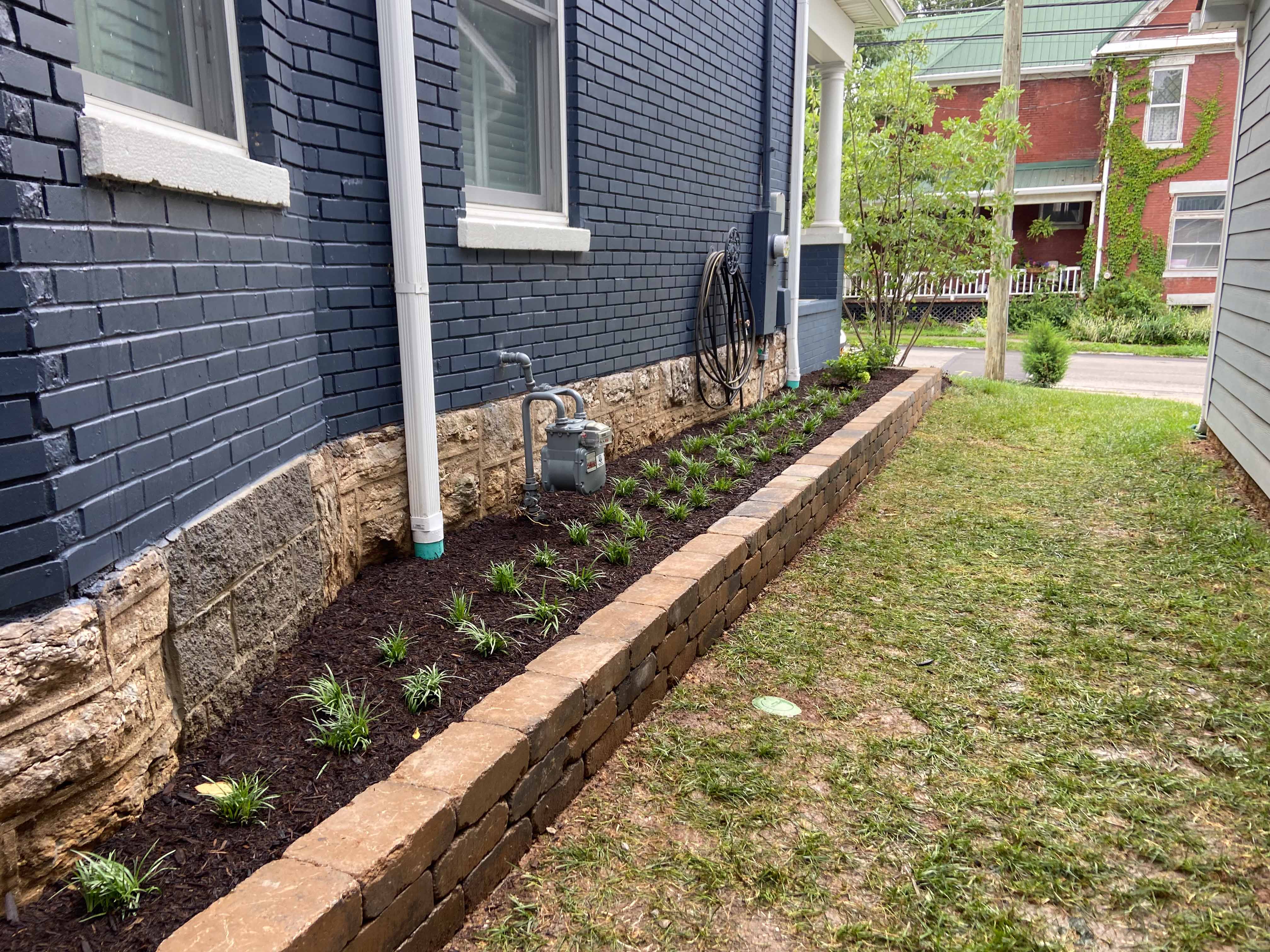 Side yard with retaining wall and liriope plants in mulch.