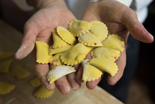 Close-up of hands holding freshly made stuffed pasta pieces dusted with flour.