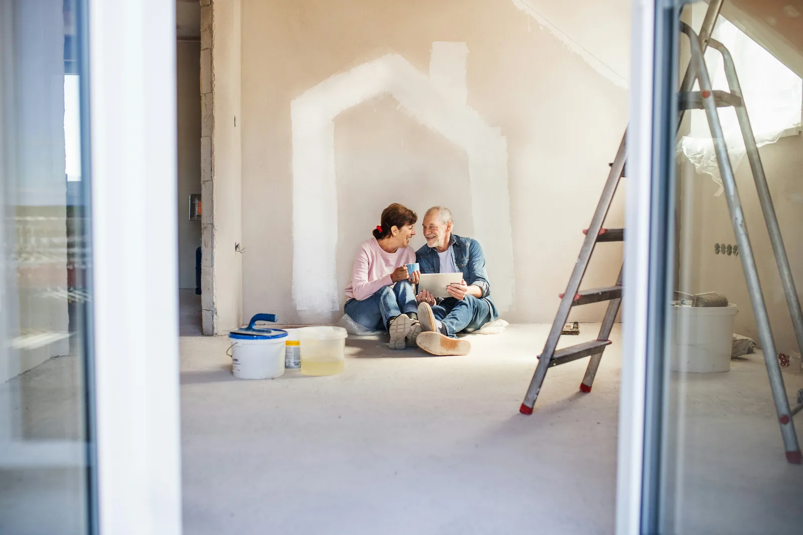 Couple sitting on floor planning renovation with tablet and ladder