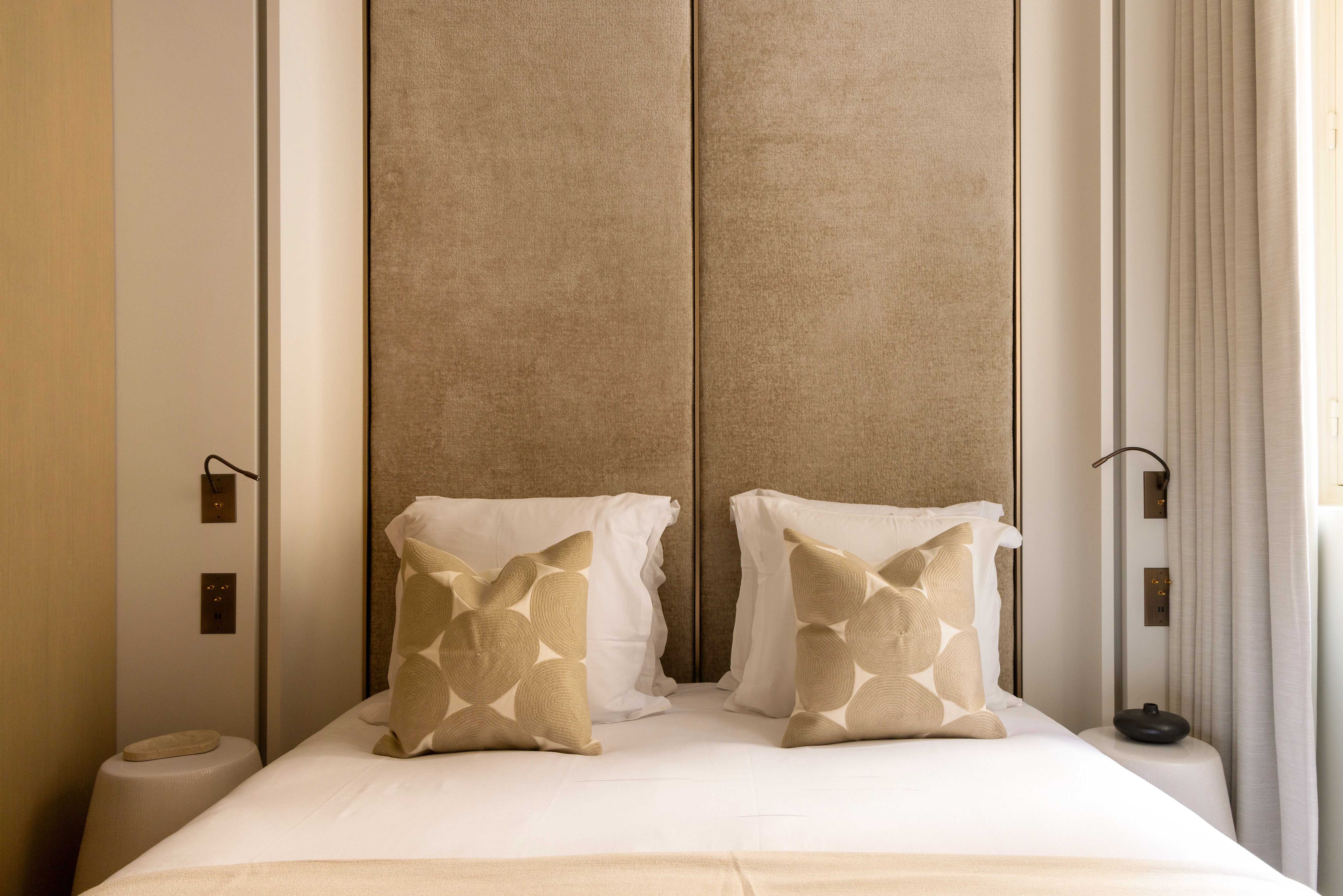 Lit double avec tête de lit velours beige encadrée de panneaux, coussins graphiques et liseuses noires