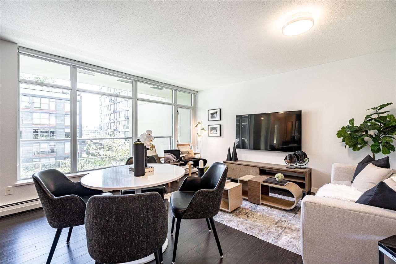 Modern living room with a dining area, large windows, plants, and stylish furniture in a bright, open space.