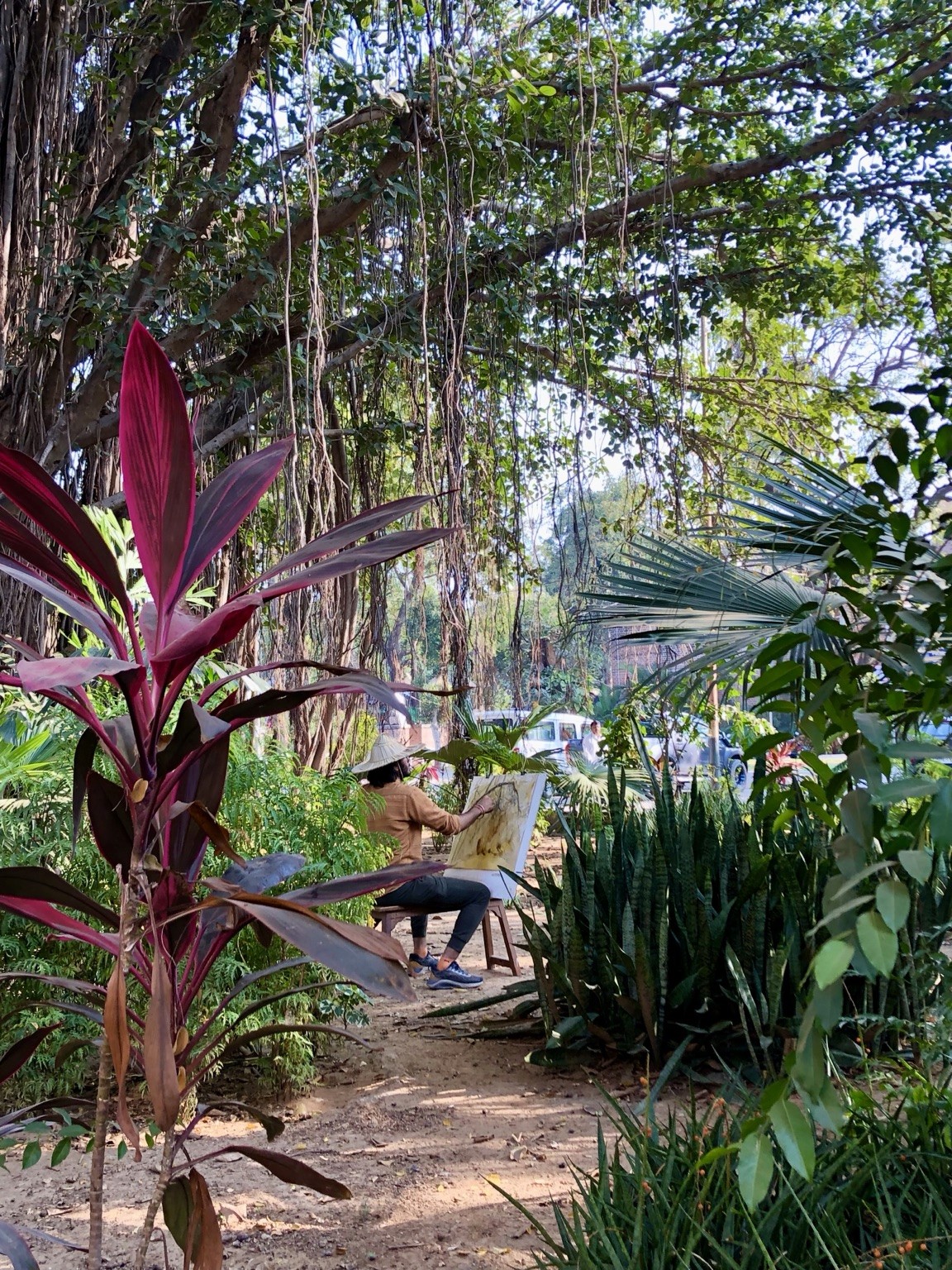 A painter sitting amid tropical greenery and magenta leaves. Photograph by Pranjali Shah.