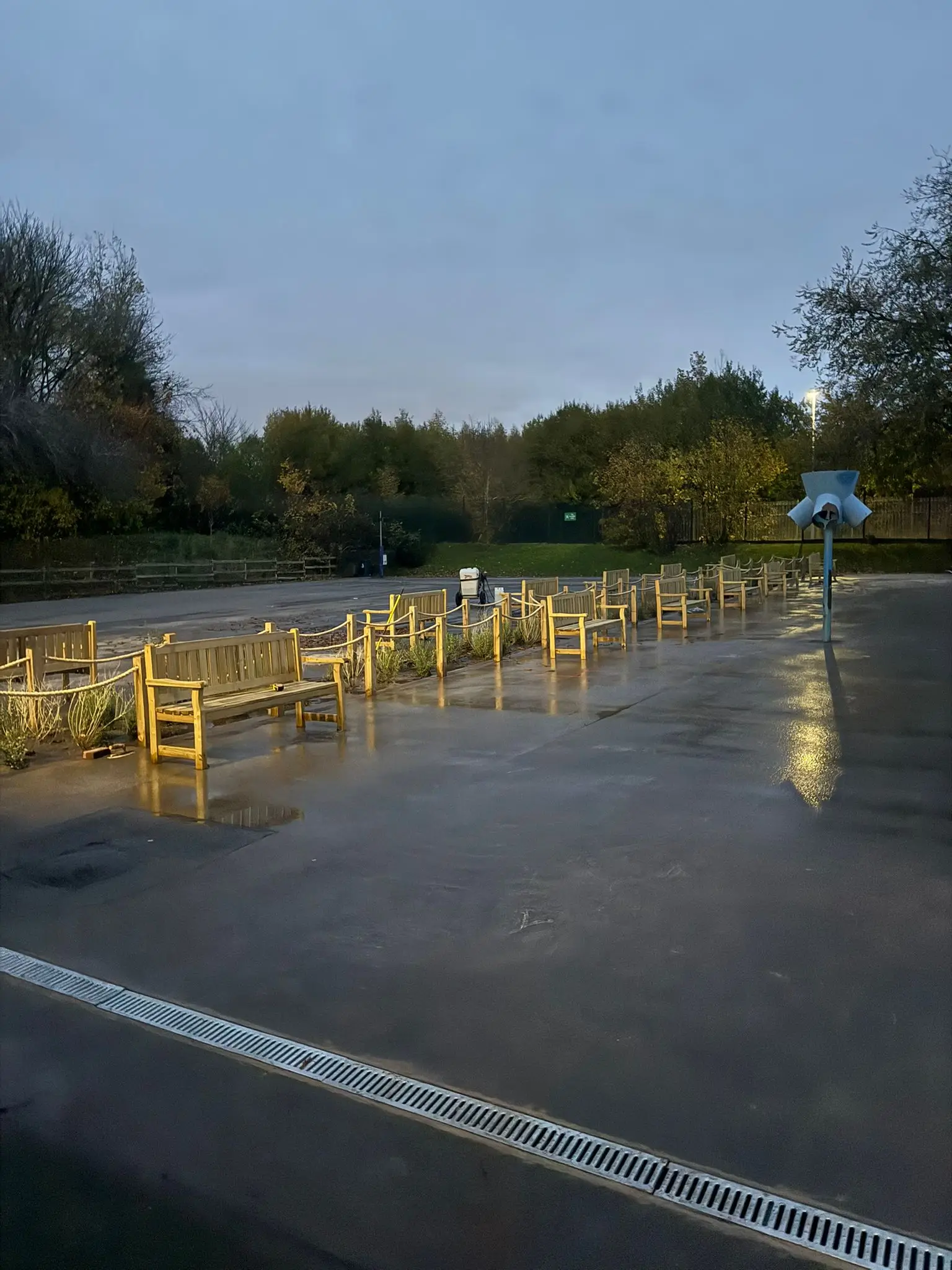 A quiet, wet road with a yellow barrier and trees in the background under a cloudy sky.