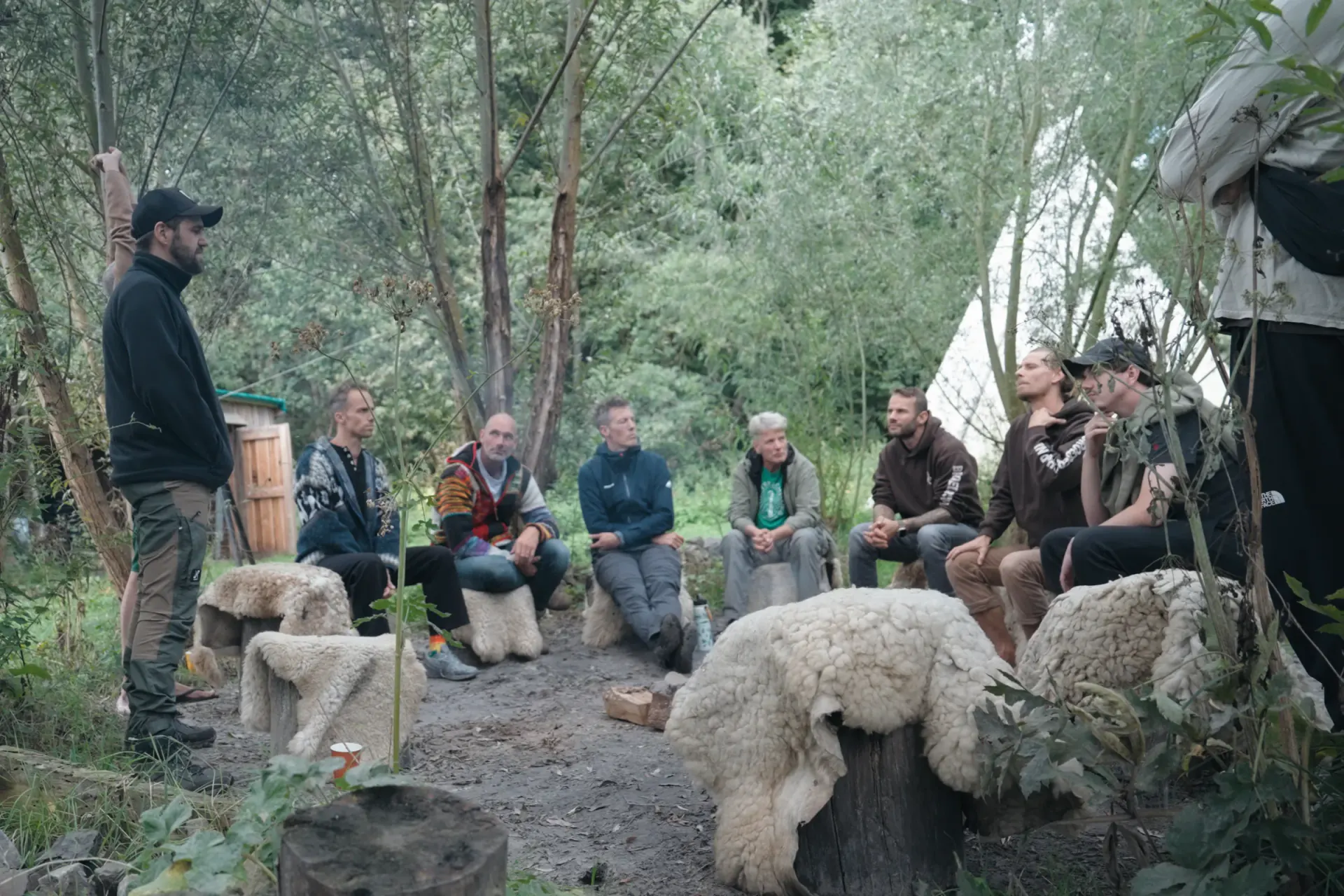 Mannen zitten in een cirkel op schapenvachten bij een tipi aan het begin van de eerste Quest