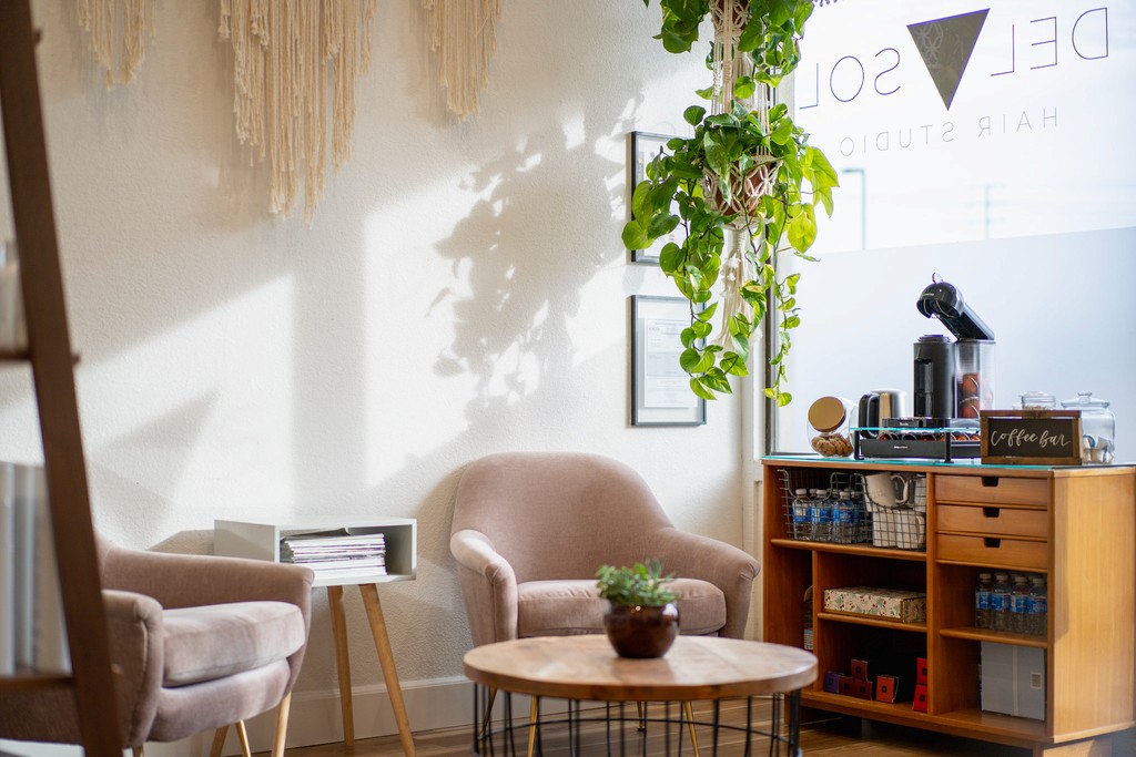 Cozy coffee bar at the entrance of Del Sol Hair Studio, featuring soft seating, hanging greenery, natural light, and a curated beverage station for guests.