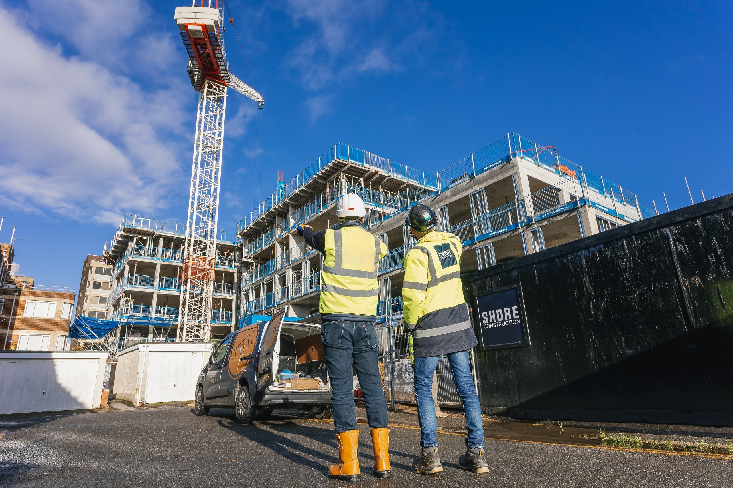 2 construction managers wearing PPE looking up at a construction site with a tower crane and hoardings