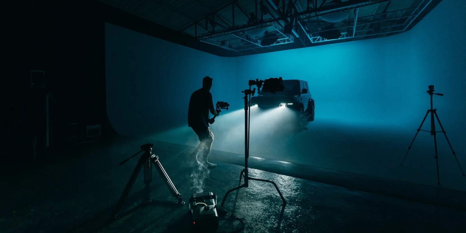 Camera operator with a gimbal filming the Chery V23 headlights through smoke in teal light