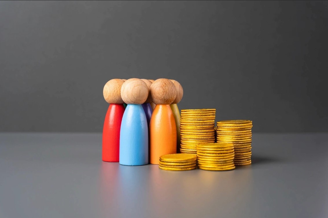 Wooden models of people next to a stack of coins. 