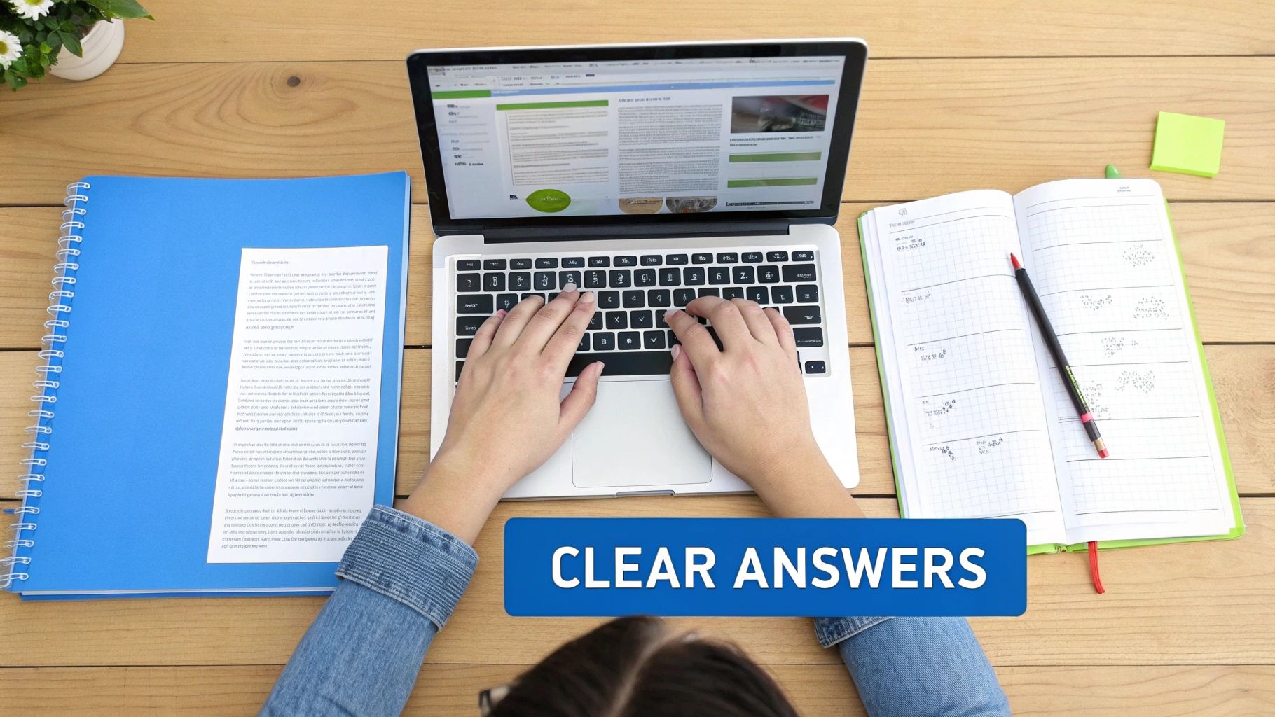 Overhead view of a person typing on a laptop, surrounded by study materials on a wooden desk.