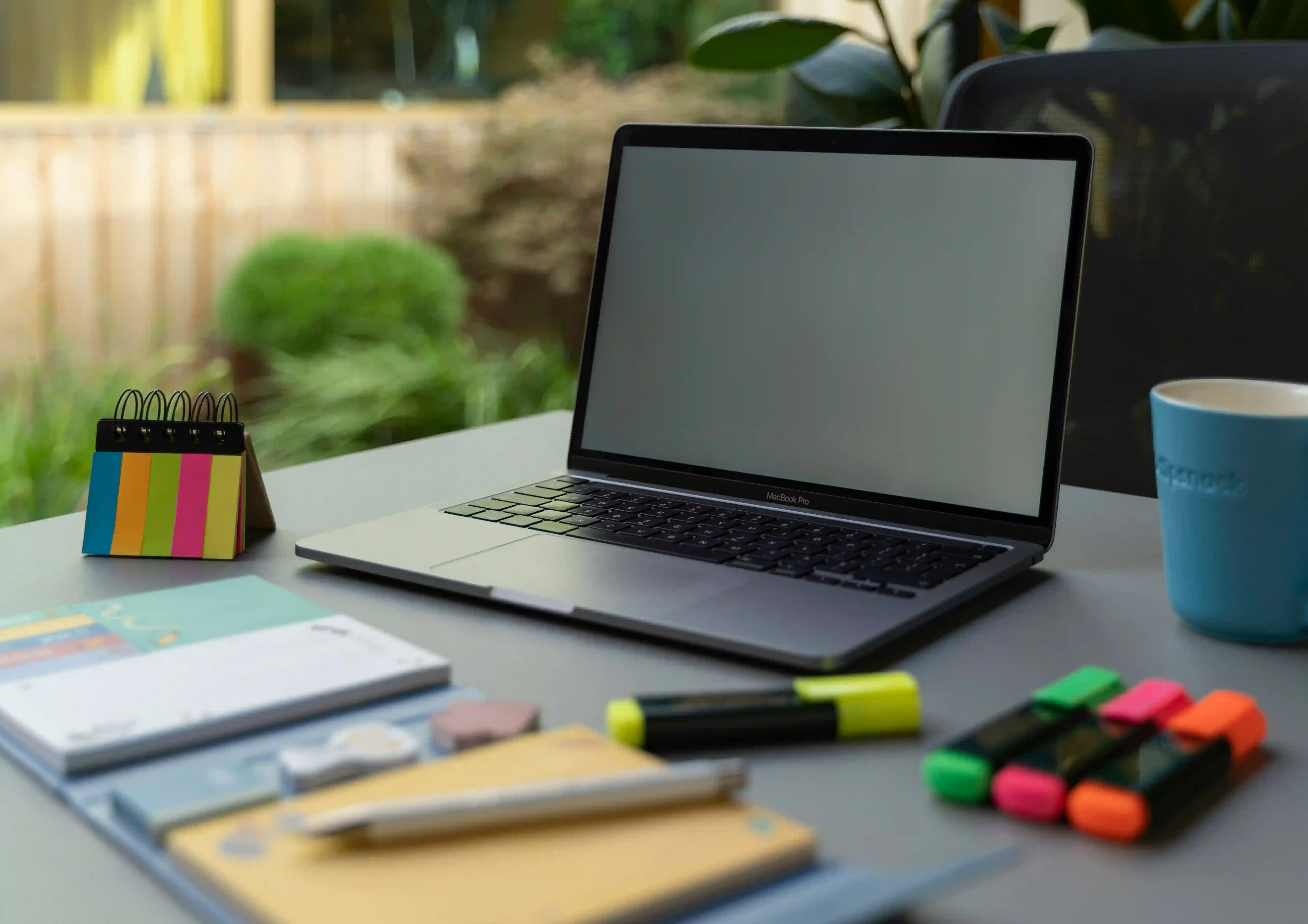 A desk with a laptop, keyboard, phone and a cup of pencils