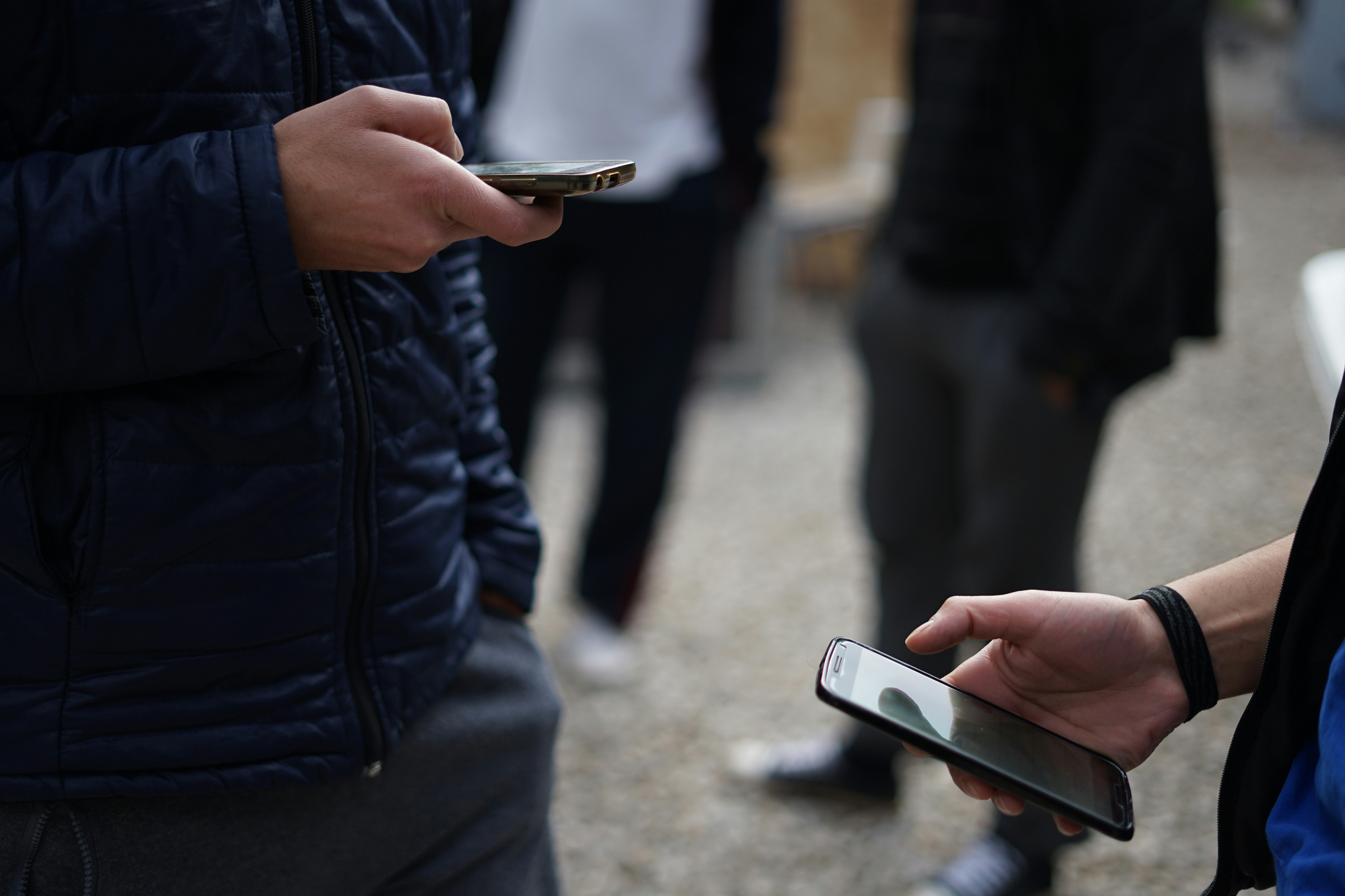 Two people holding smartphones while standing outdoors.