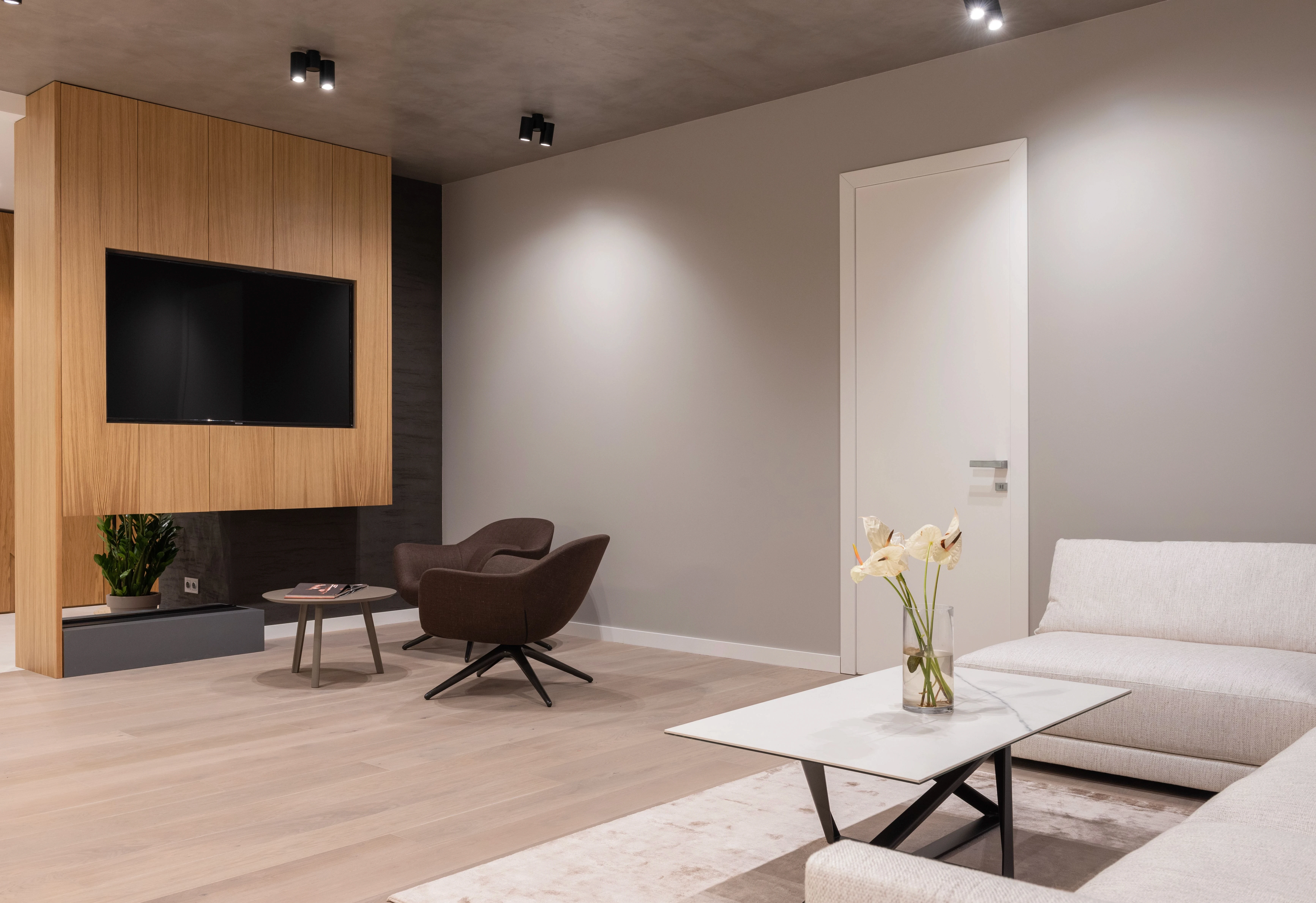 Minimalist modern living room featuring a wall-mounted television panel, stylish armchairs, and white sofas.