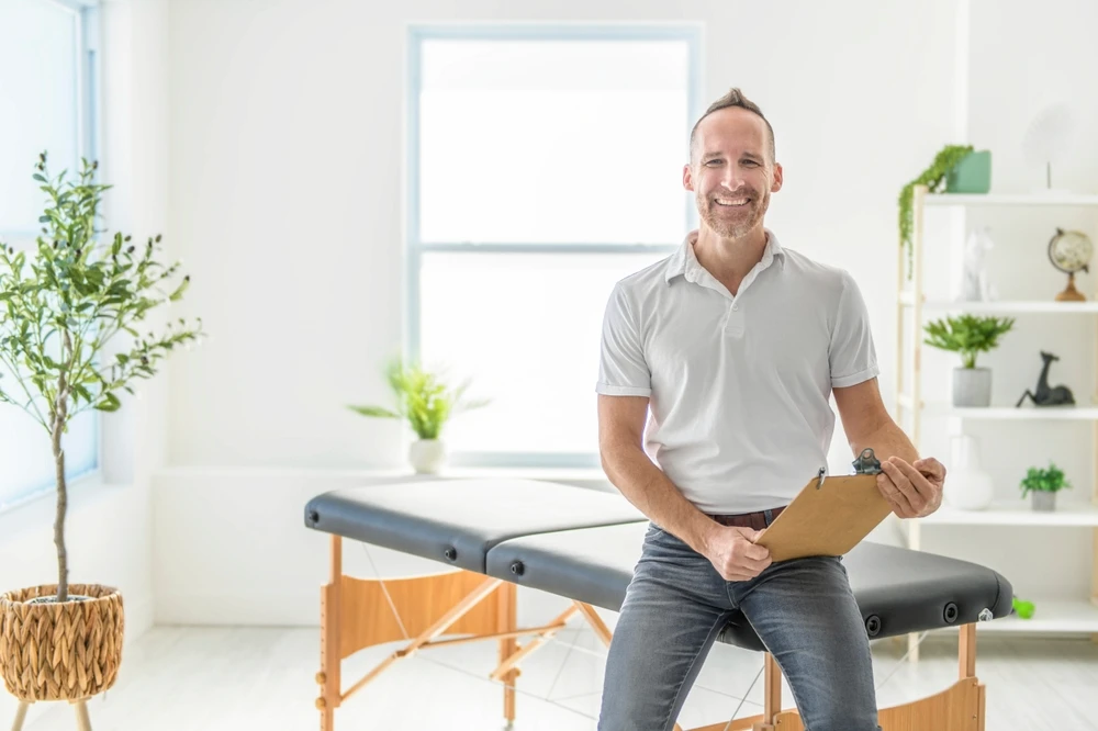 A smiling chiropractor holding pad in hospital and looking at camera
