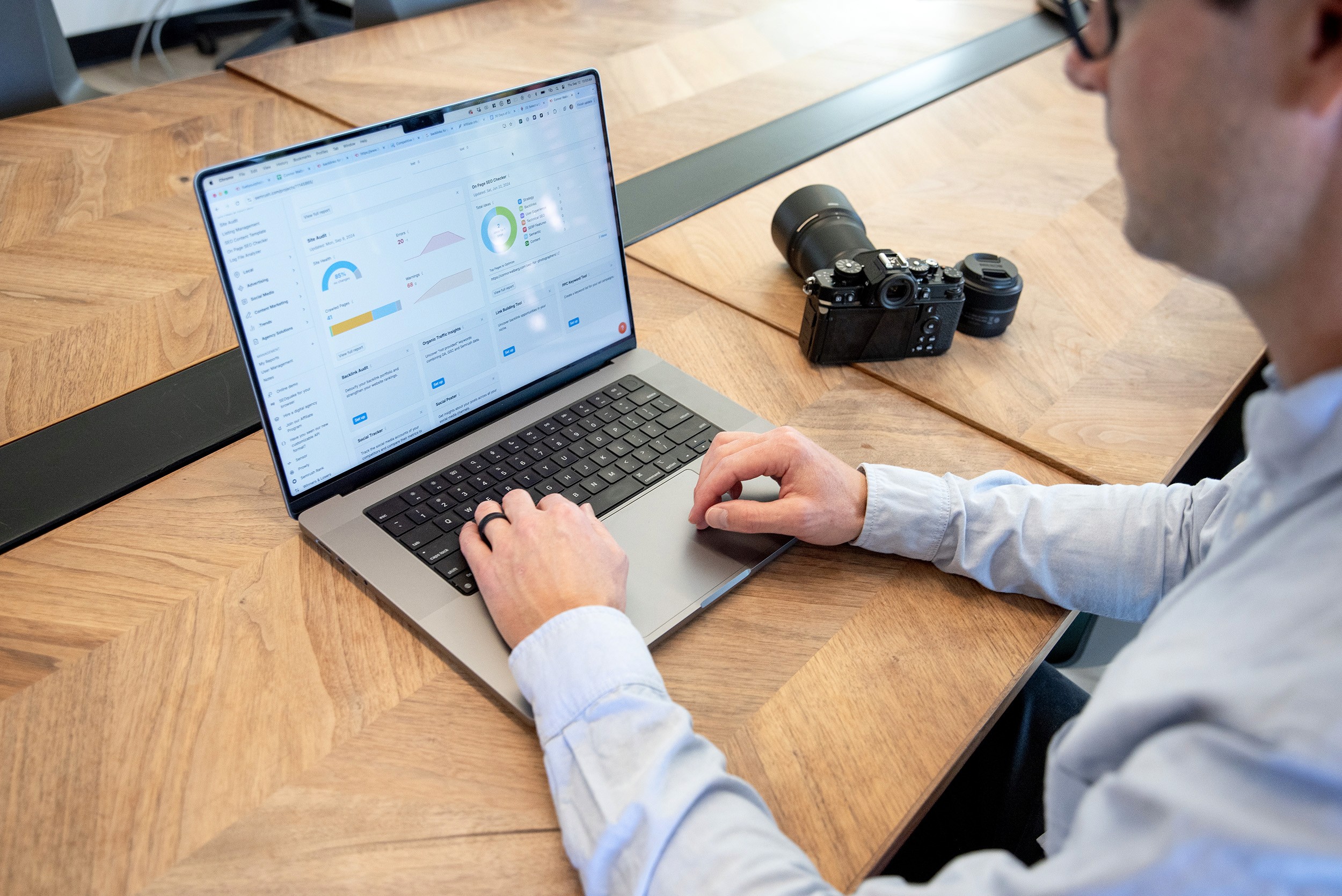 Photographer sitting at modern desk working on website seo with camera and lens