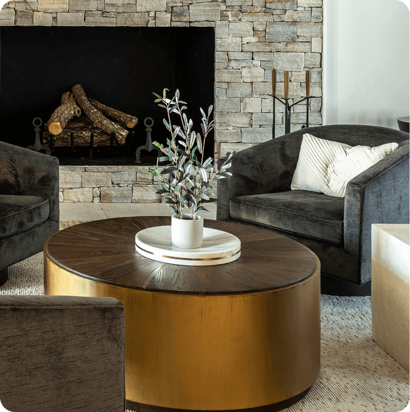 Modern sitting room with round brass coffee table, gray sectional sofa, and stone fireplace with decorative logs