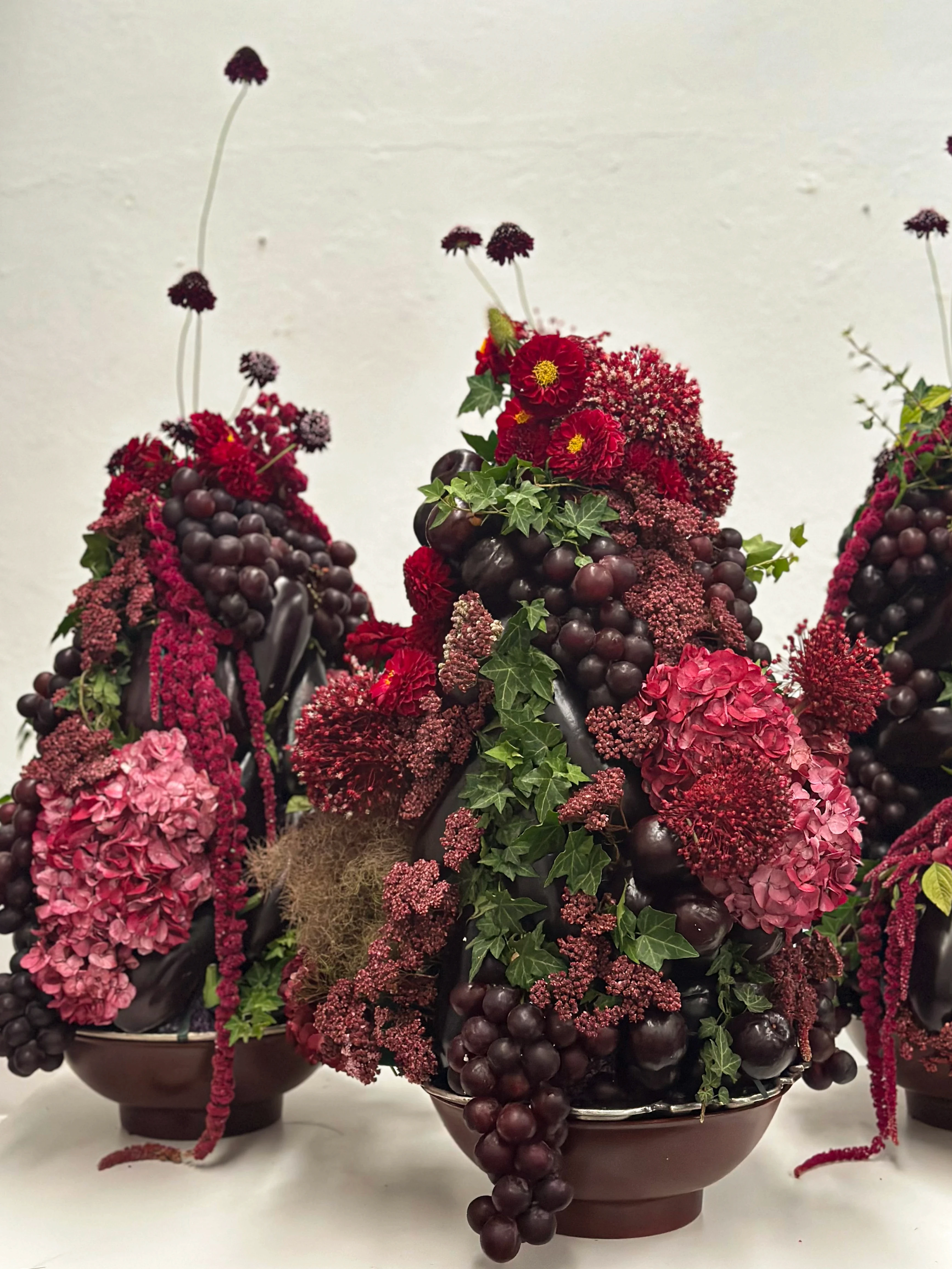Primer plano de arreglos barrocos mezclando flores bordó, frambuesa, hiedra y frutas frescas.