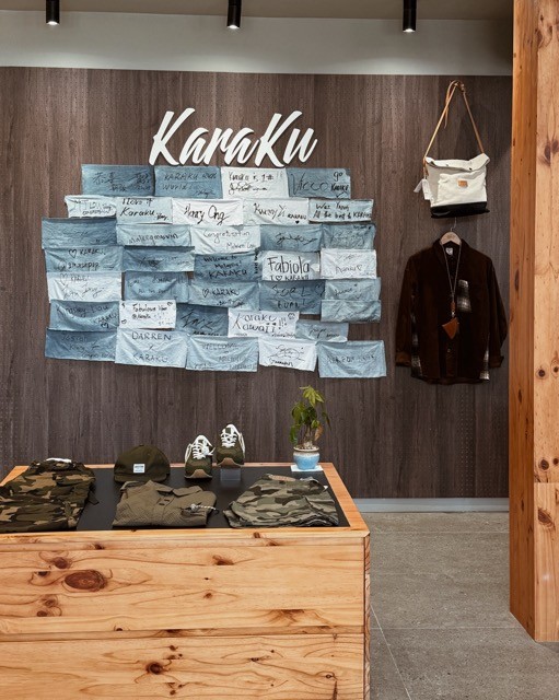 Interior of a retail store featuring 'Karaku' signage, denim patch wall display, and various clothing items on a wooden table.