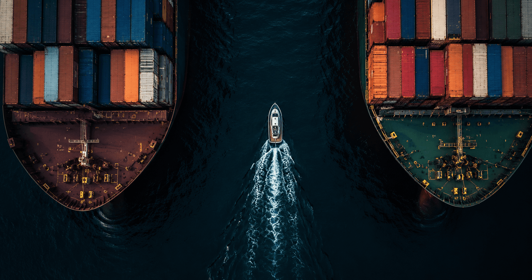 Aerial view of a small agile vessel navigating confidently between massive cargo ships on dark open water