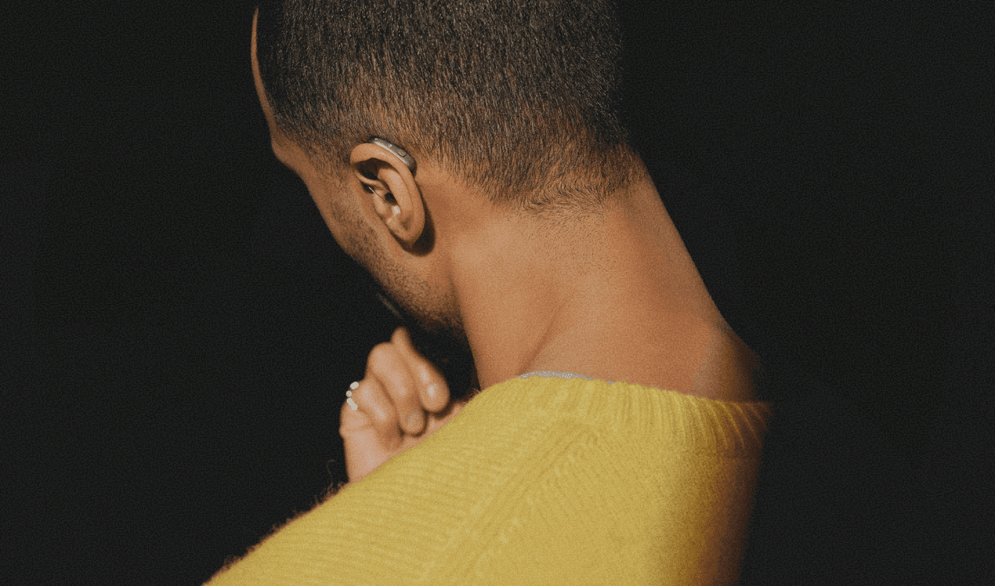 Portrait of a figure turned away from the camera in low warm lighting.