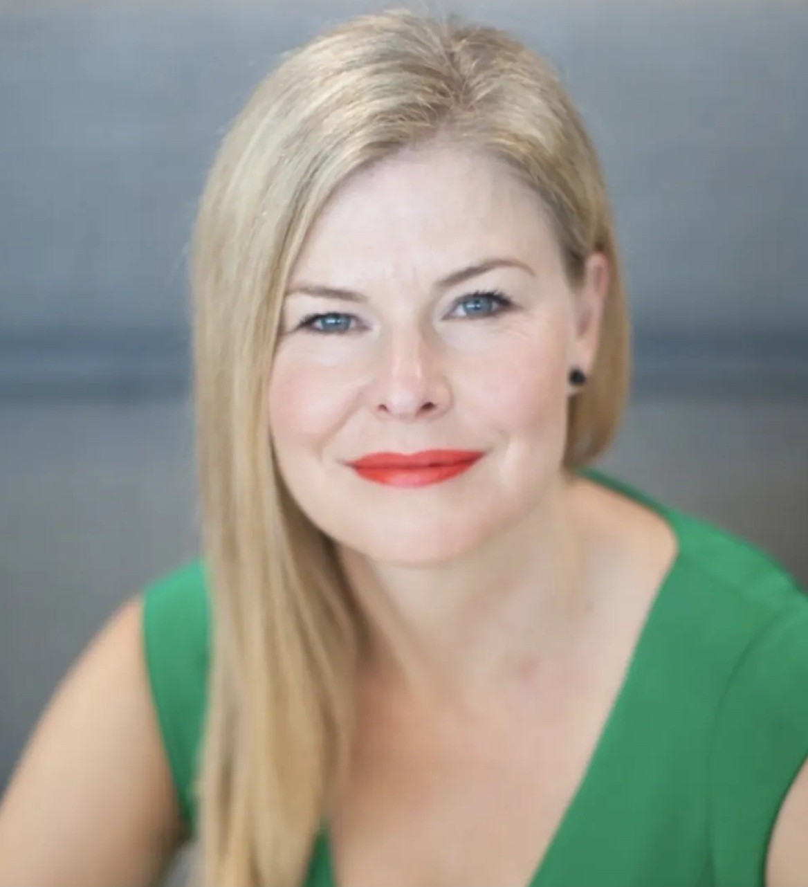 Smiling woman in beige linen outfit standing indoors with plants and books in the background.