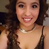 Portrait of a smiling person with curly hair, wearing a necklace and a black lace top.