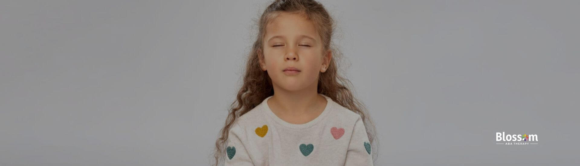 A girl with autism is sitting cross-legged on the floor, eyes closed in a meditative pose.