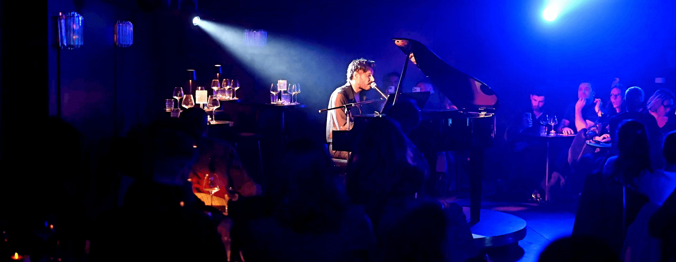 A musician plays a grand piano on a stage with dramatic blue and white spotlights, creating an atmospheric, performance-ready scene.
