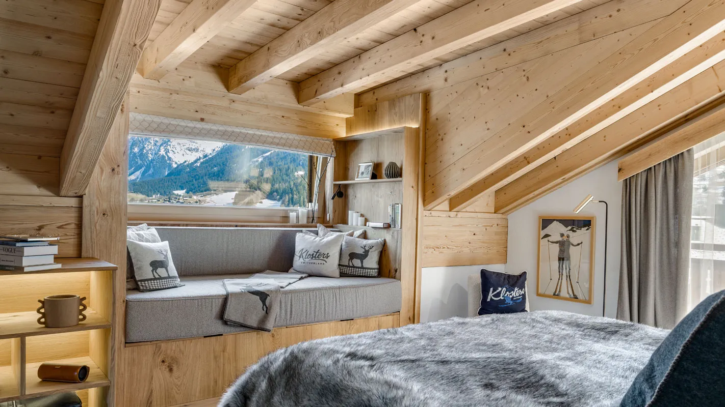 Silvretta Klosters bedroom with a window seat, exposed timber beams, and panoramic Swiss Alps views