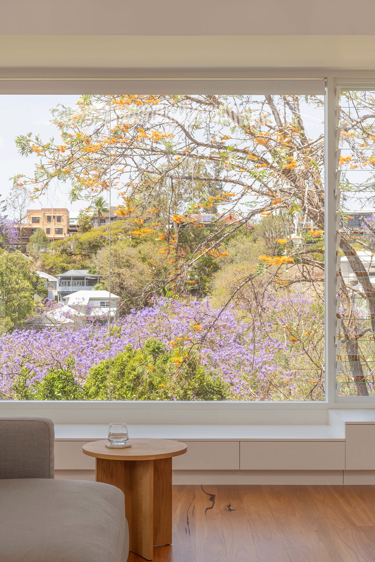 Living room window framing jacaranda trees in bloom, with a built-in bench, timber floors, and soft afternoon light.