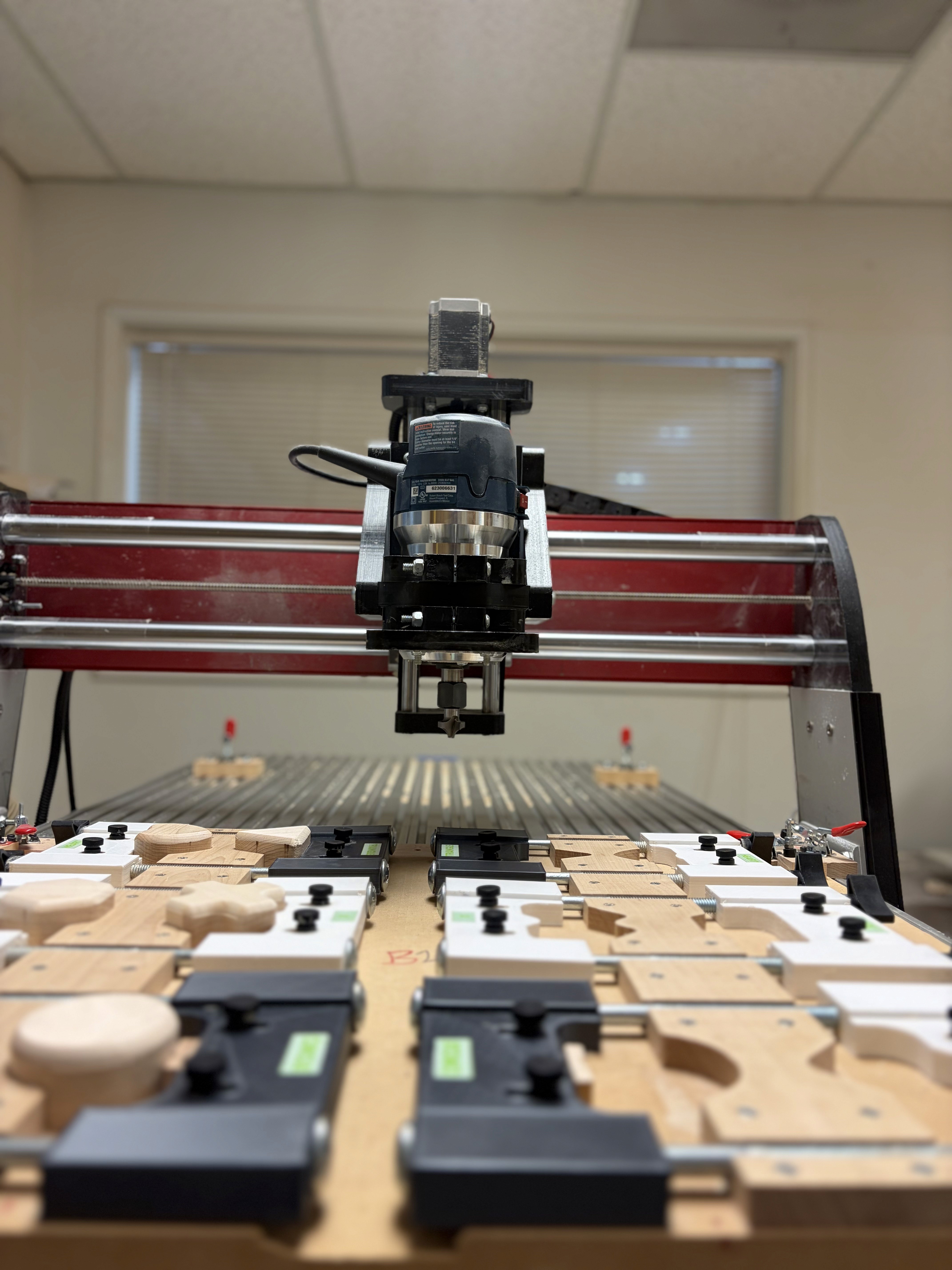 A CNC router above a jig bed of clamped wooden toy parts