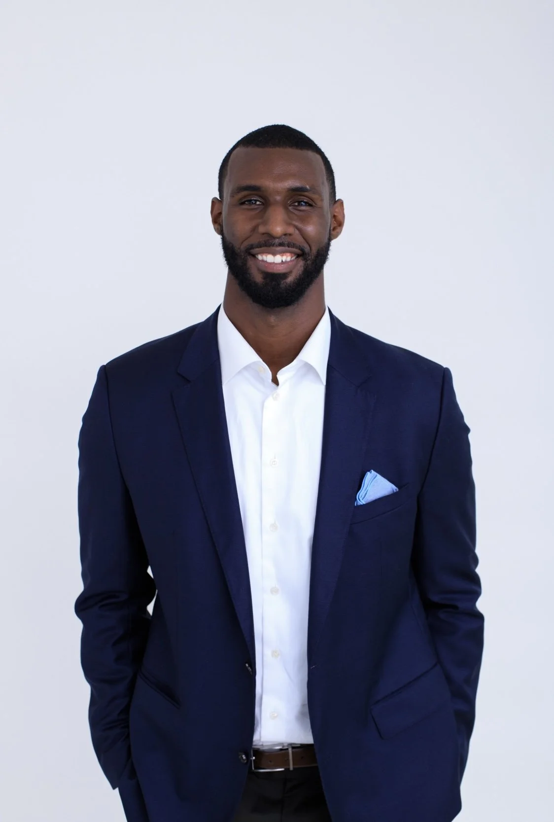 Asante Cleveland in a navy suit, smiling in a studio portrait