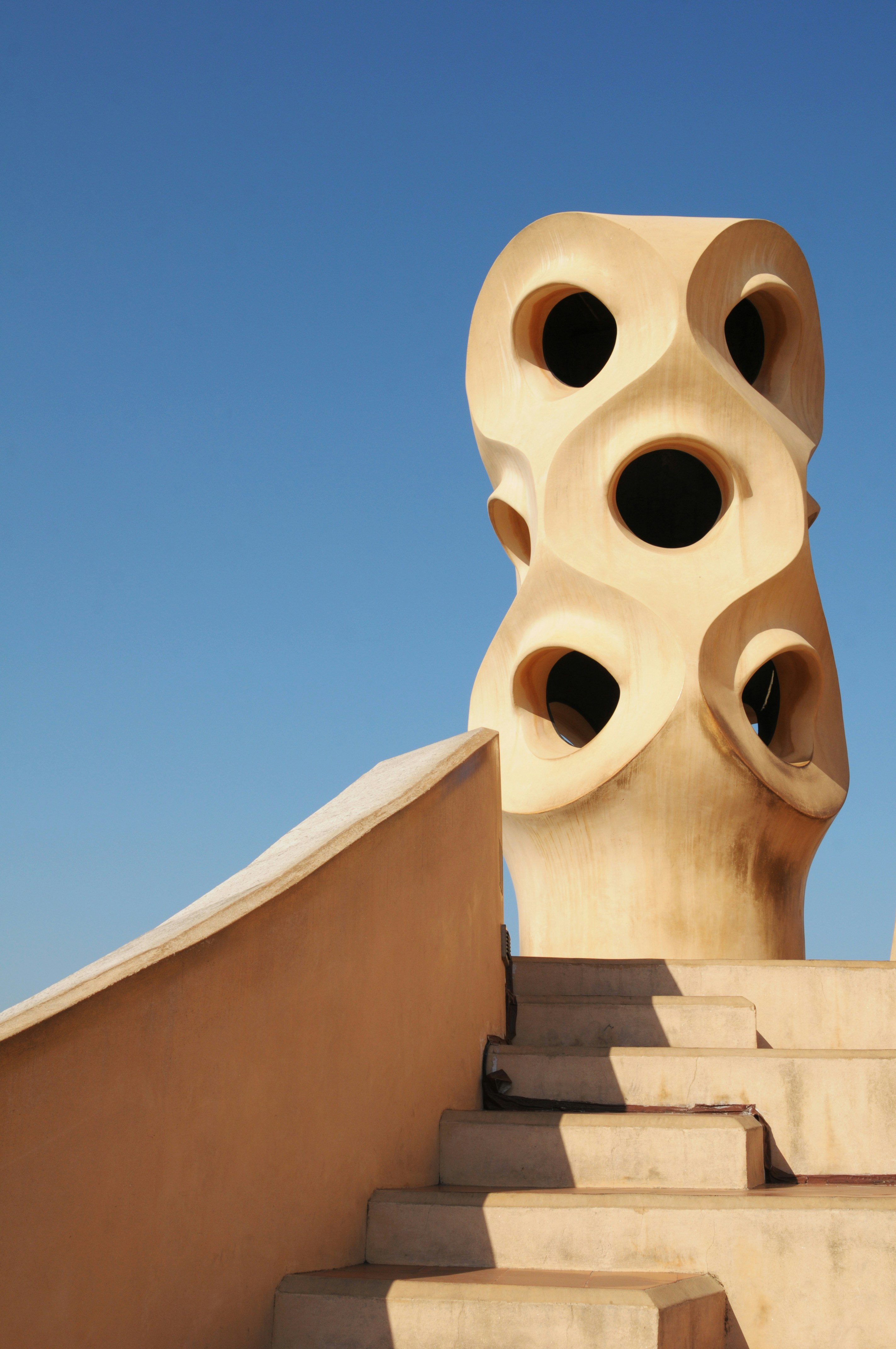 A biege abstract sculpture with several strange holes at the top of a staircase on the roof of the Casa Mila in Barcelona.
