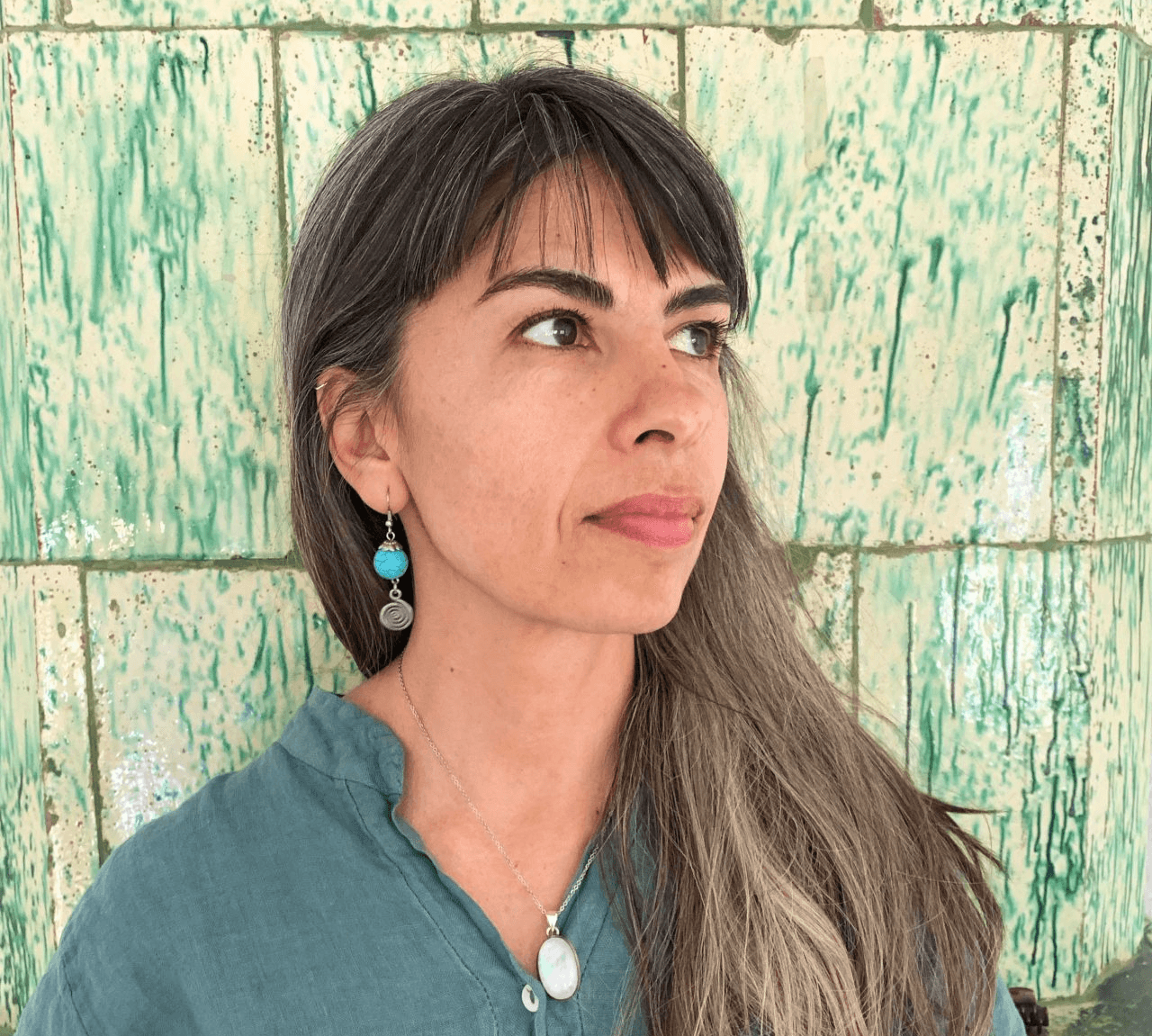 Maria's portrait.  She is wearing a blue top and earrings stands in front of a green-patterned background.