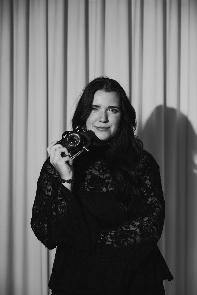    South Florida wedding photographer Makaela Skinner holding a film camera in a black and white self portrait outdoors.