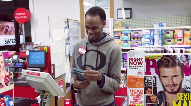 A photo of a man holding a phone while sitting in a store near a cash register.