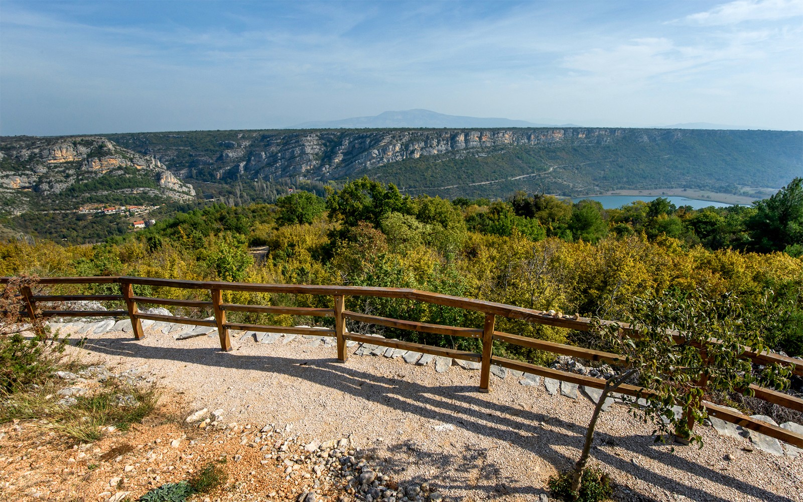 View from a wooden railing at Krka National Park overlooking lush greenery and distant cliffs.