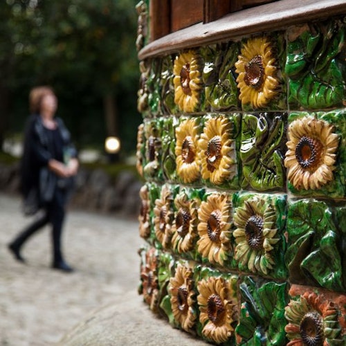 Close-up of a wall adorned with ceramic sunflower tiles. A person in dark clothing is blurred in the background.