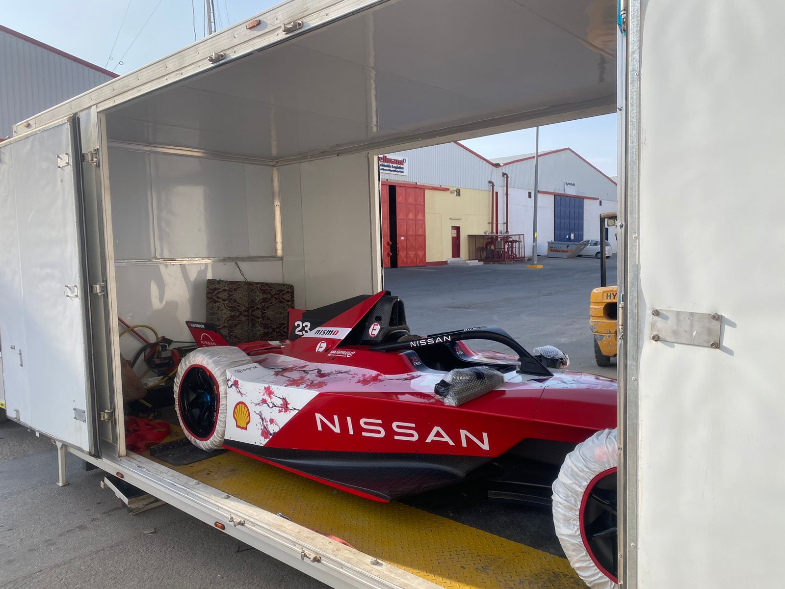 Extra Space car shipping of a red and white Formula E race car loaded into an enclosed white trailer outdoors.