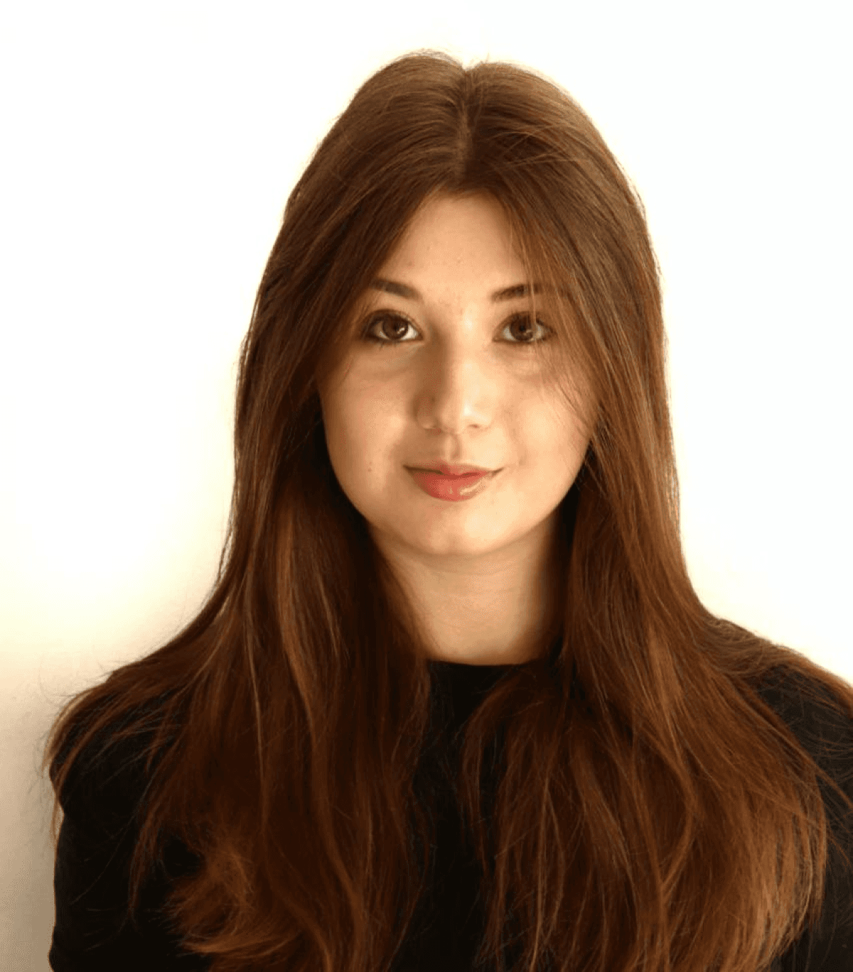 A young woman with long brown hair poses against a plain white background, wearing a black top.