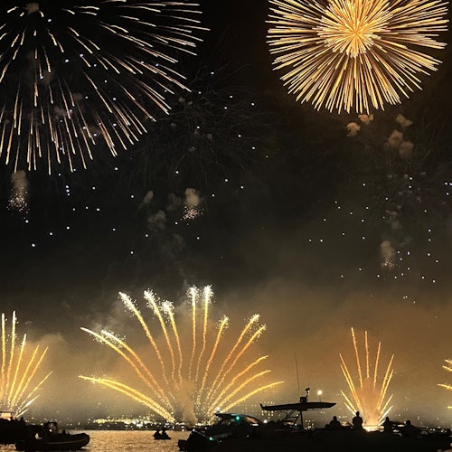 Fyrverkeri lyser opp nattehimmelen over vannet med båter i forgrunnen.