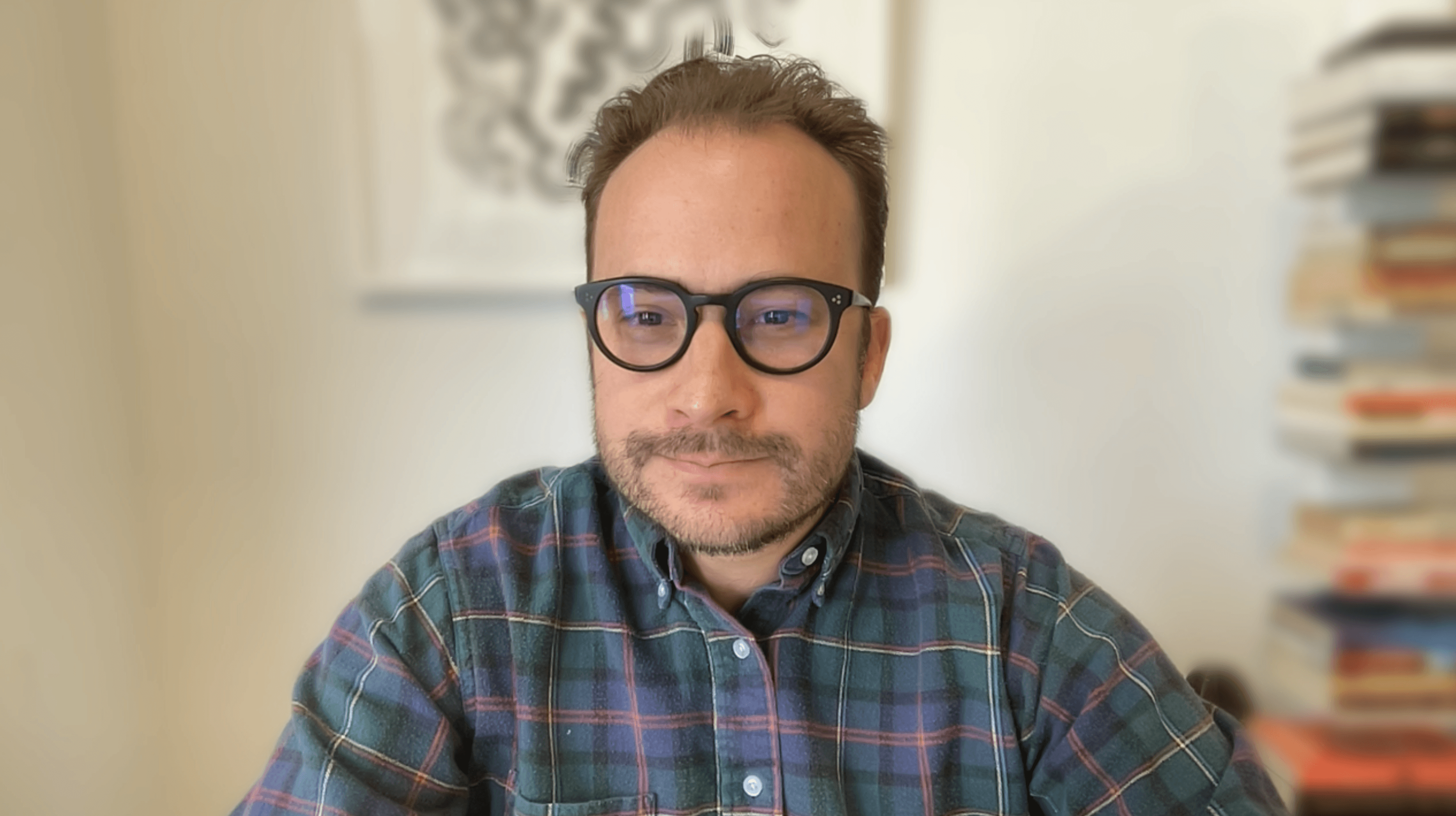 Person wearing a blue puffer jacket and red backpack standing in front of a light blue building on a city street.