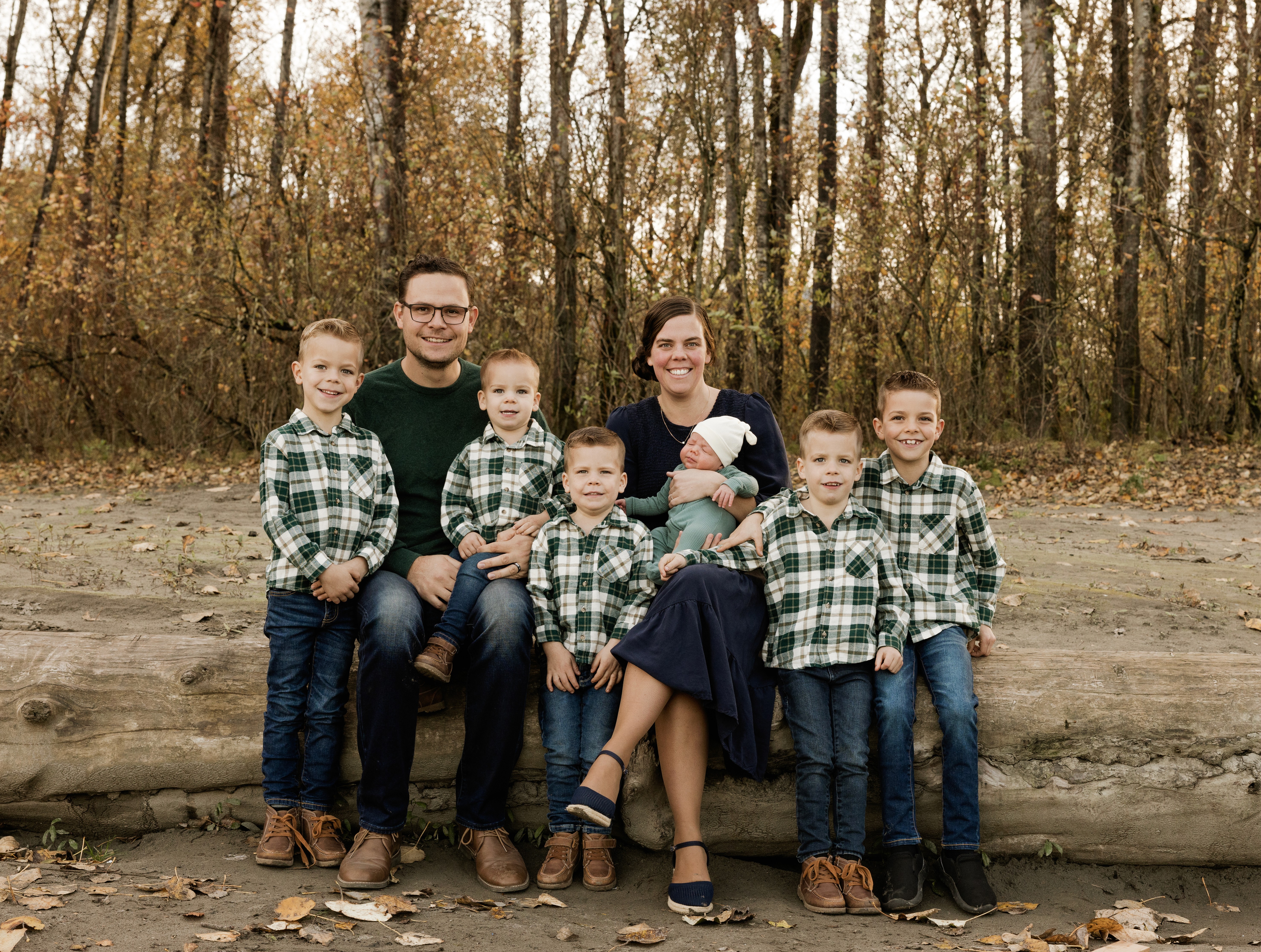 A young person with curly hair smiles at the camera while sitting in front of a laptop against a dark background.