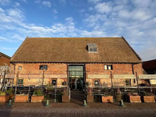 The historic red brick exterior of Marriott's Warehouse under a bright blue sky with scattered clouds, featuring outdoor seating and planters out front.